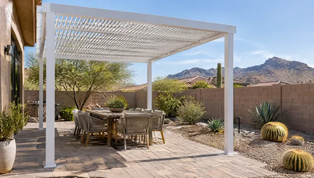 Freestanding white powder-coated aluminum pergola with slim lattice rafters over a paver patio in a Phoenix backyard, outdoor dining set, gravel landscaping with barrel cactus, stucco block wall