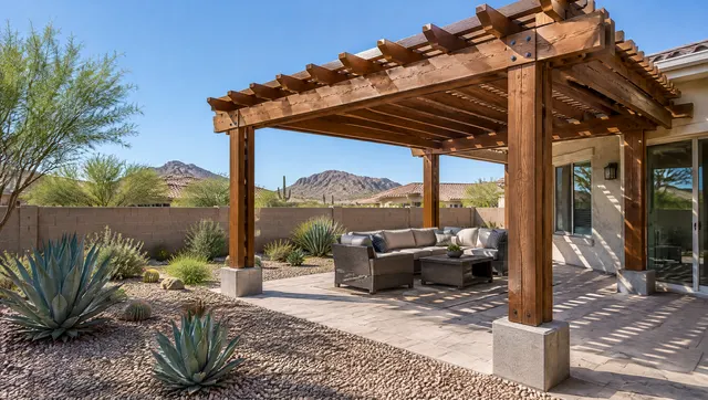 Freshly built pergola in a Phoenix backyard: stained wood posts on concrete footings, doubled beams and rafters over a patio, gravel and agave landscaping, block wall, clear blue sky
